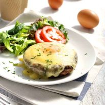 Baked Eggs in Mushrooms covered in melted cheese on a white plate with coffee on the side, ready to be eaten.