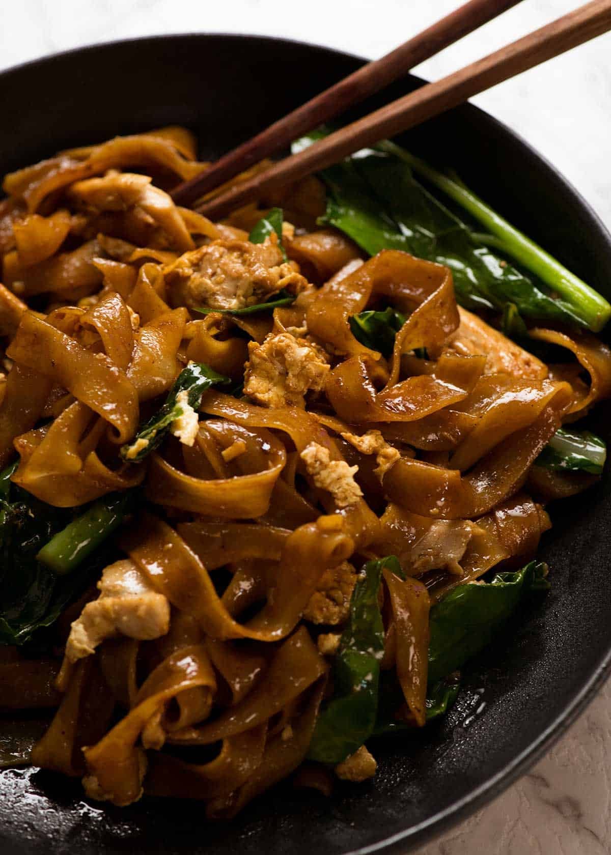 Close up of Pad See Ew noodles on a plate with chopsticks, ready to be eaten