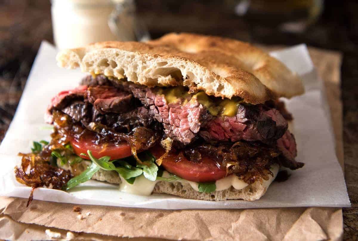 A juicy Steak Sandwich loaded with tender slices of steak, caramelised onion, garlic aioli, lettuce, tomato and mustard. staging.recipetineats.com