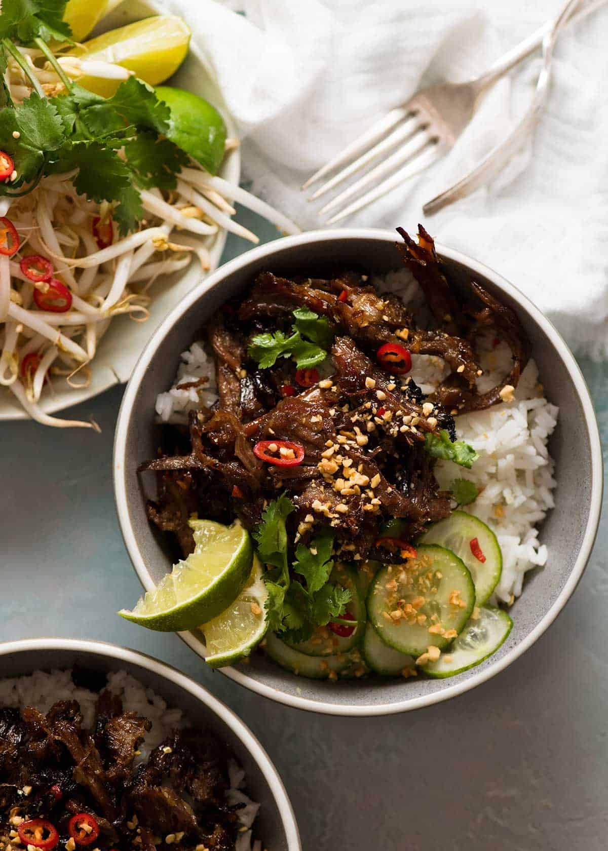 2 bowls of Caramelised Vietnamese Shredded Beef over rice with a side of bean sprouts and fresh herbs
