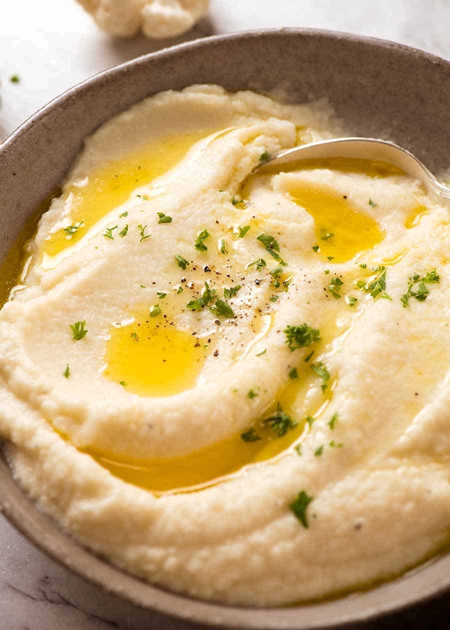 Rustic brown bowl of Creamy Cauliflower Mash topped with a drizzle of butter