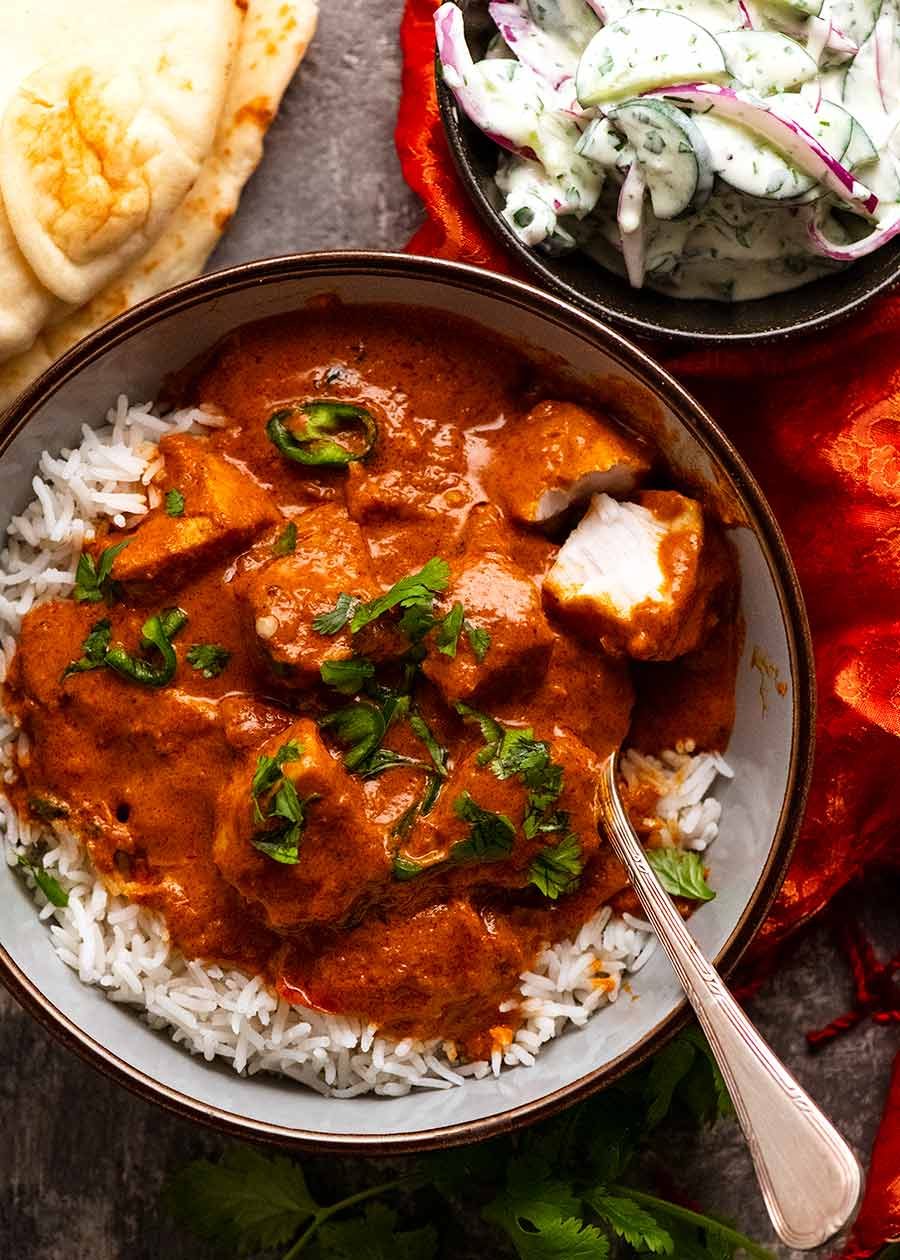 Overhead photo of Goan Fish Curry served in a bowl with basmati rice with a side of cucumber yogurt salad and naan