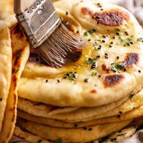 Brushing melted garlic butter on a freshly cooked naan